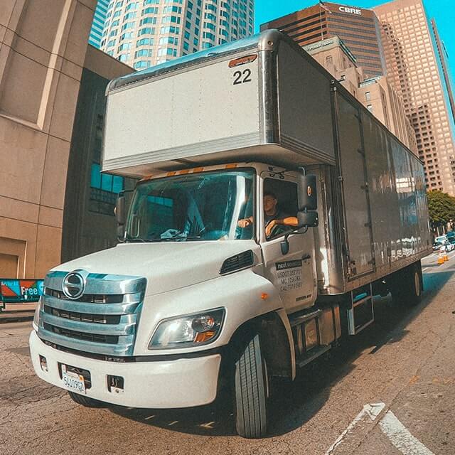 Next Moving professional office movers near me are sitting in moving box truck by the office building and waiting for the client ready to provide best moving services.