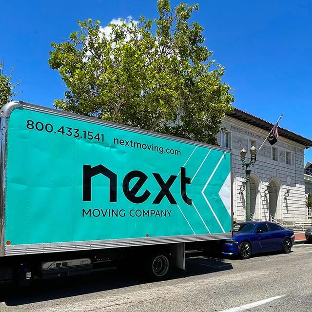 Next Moving 20-foot box truck with branded decals on it and local Glendale movers is parked by Glendale USPS office.