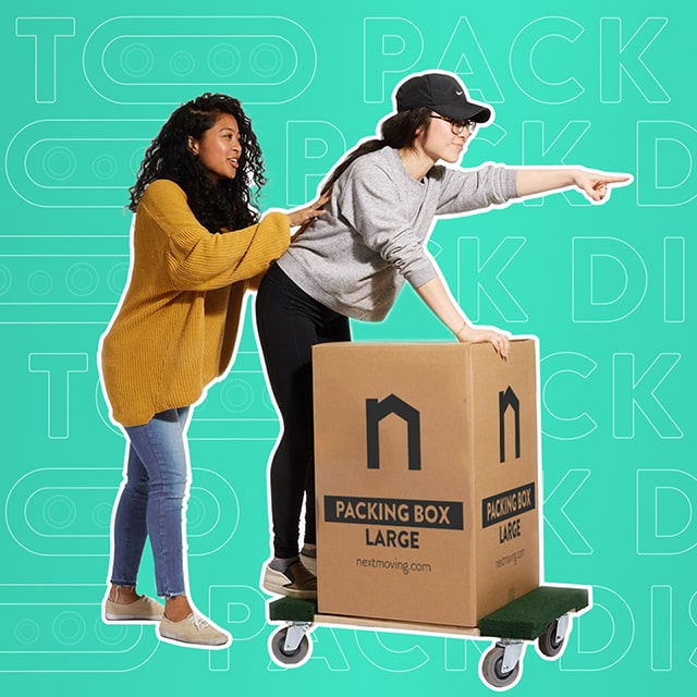 Young white woman stands on the 4-wheel dolly leaning on a large packing box with Next Moving logo on it, and pointing ahead with her index finger. The other black woman pushes her forward. This composition represents that they are confident with their packing process.