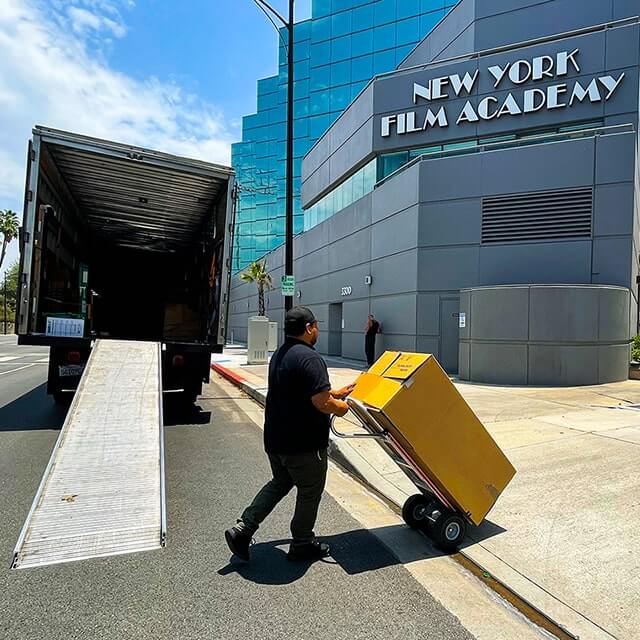 Next Moving commercial and office mover just stepped out of the moving truck ramp. He is holding a hand truck with the wardrobe box on it and moving towards the New York Film Academy Los Angeles office in Burbank California.