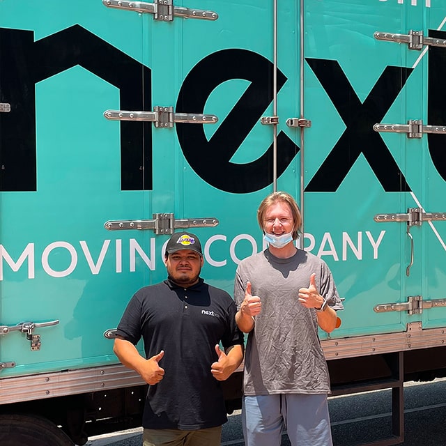 Two Next Moving professional Burbank, CA local movers standing at the front of the Next Moving truck, smiling and holding their thumbs up.
